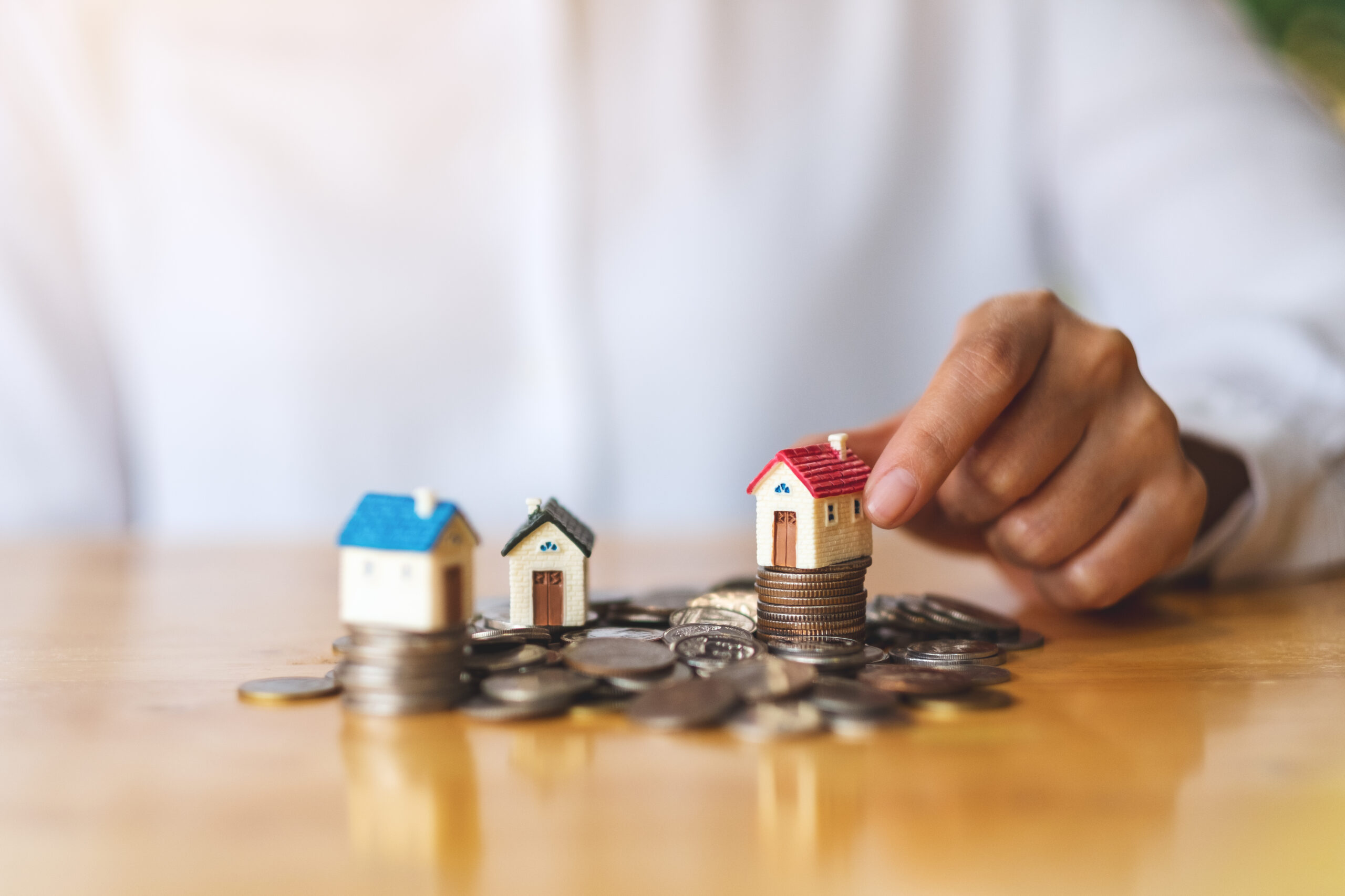 Closeup image of a woman's hand putting house model on pile of coins for saving money concept